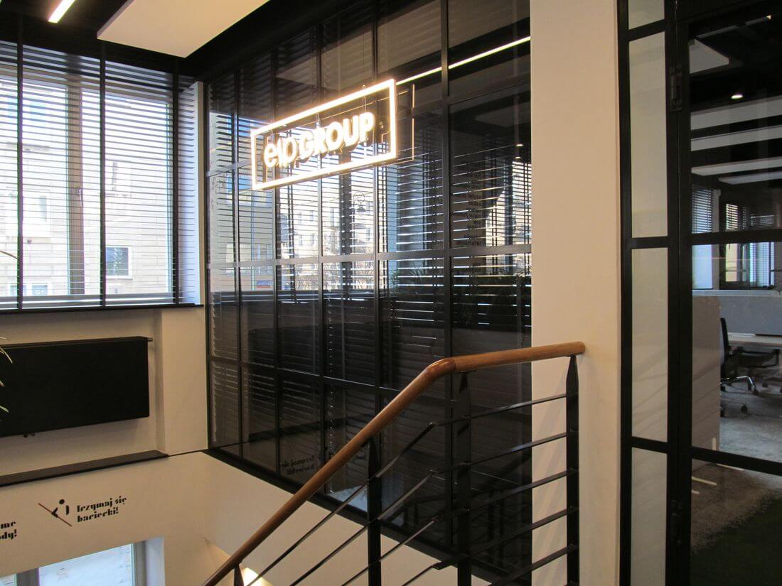 Sistema de paredes del vidrio y hierro que separa las oficinas de caféteria con el logo de neón EIP Group