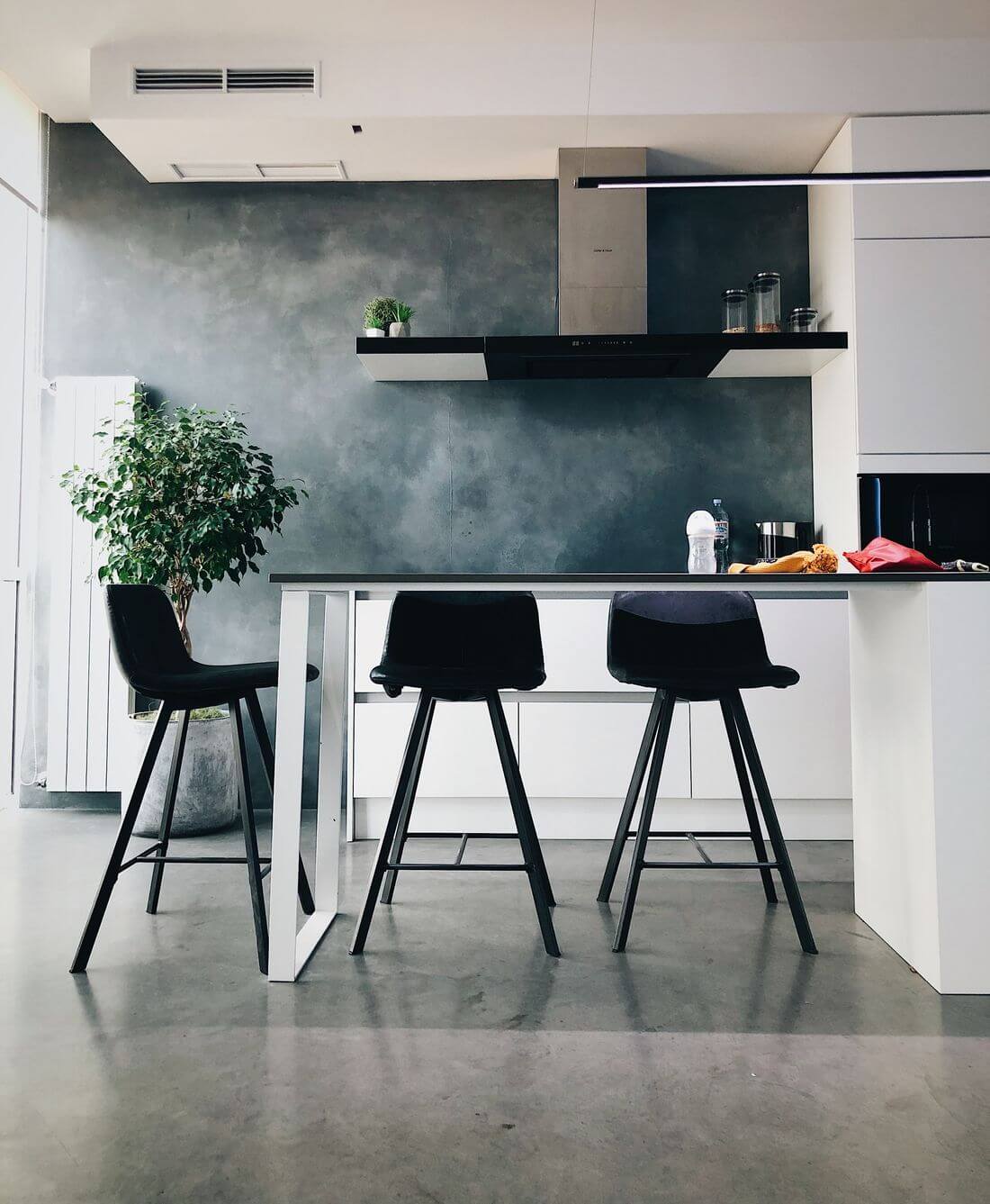 Cocina industrial de estilo loft con sillas negras altas, muebles blancos y pared de hormigón en bruto